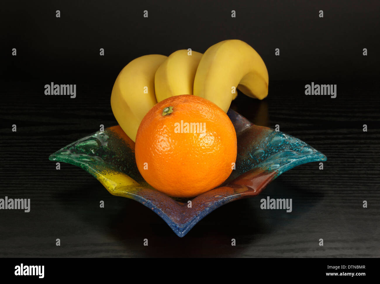 Bananen und Orange in farbigem Glasschüssel Stockfoto