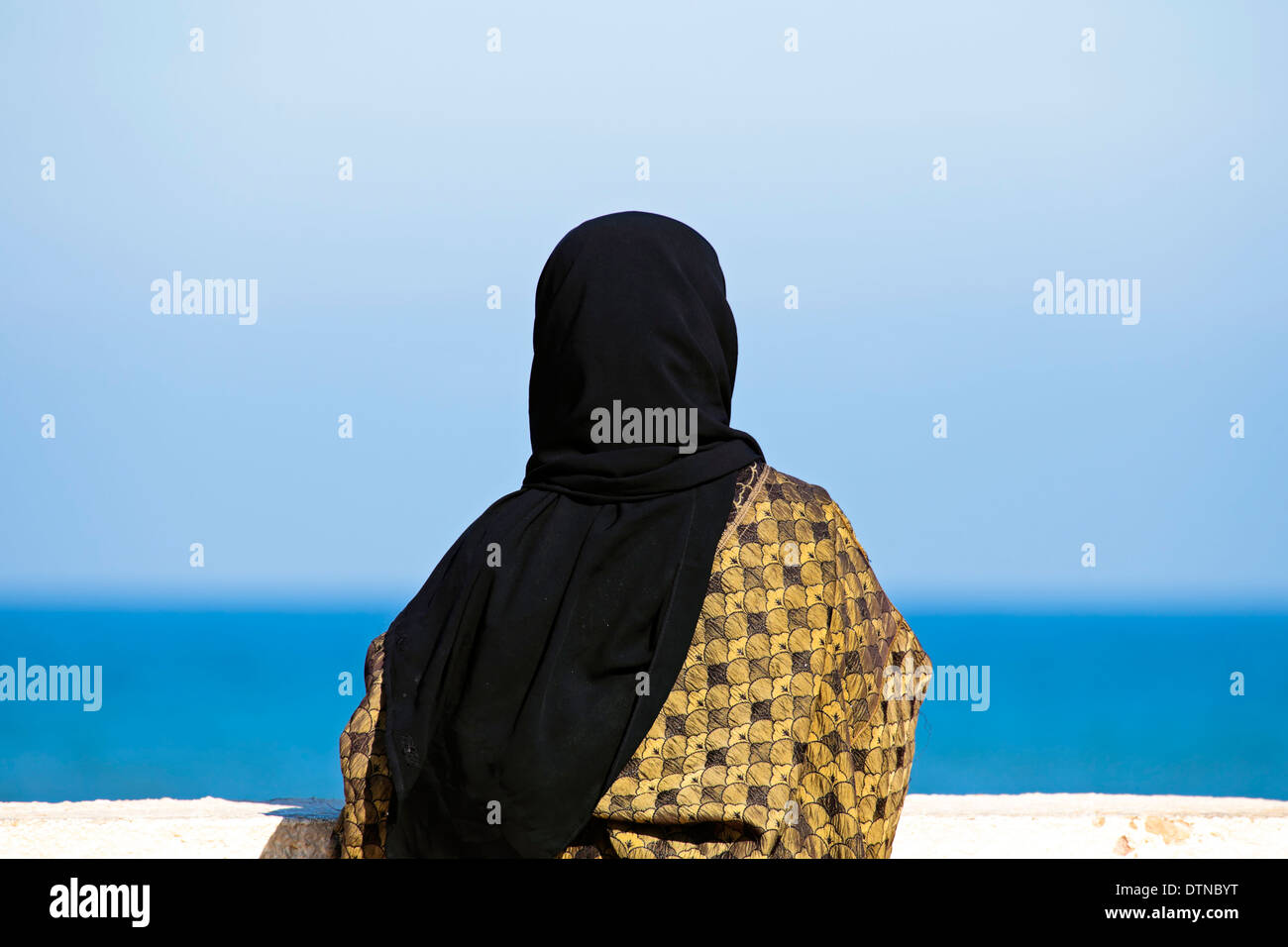 Arabische Frau mit islamischen Kopftuchs mit Blick auf den Ozean Stockfoto