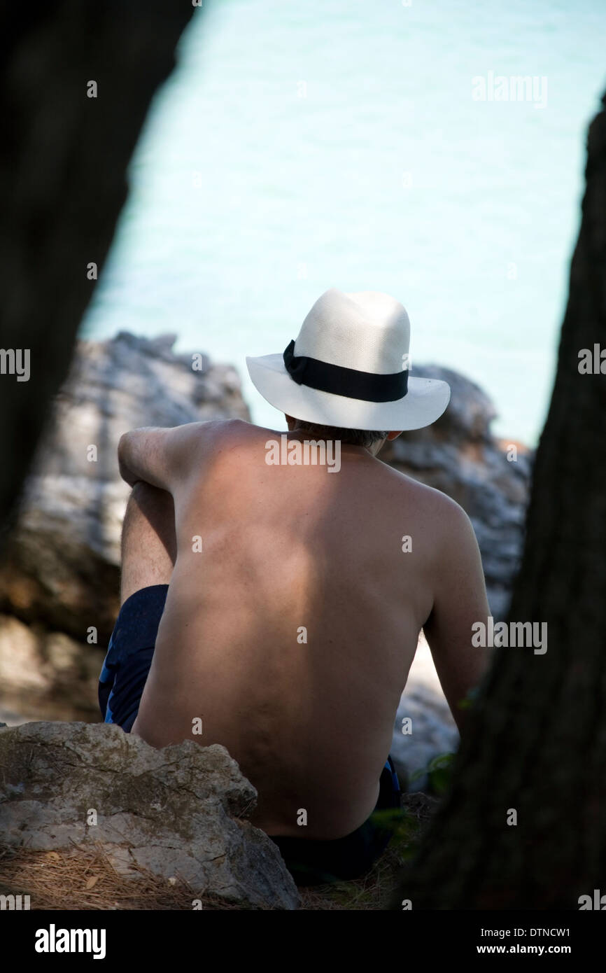 Mann sitzt auf den Felsen am Meer Panama Hut gesehen aber Bäume Stockfoto