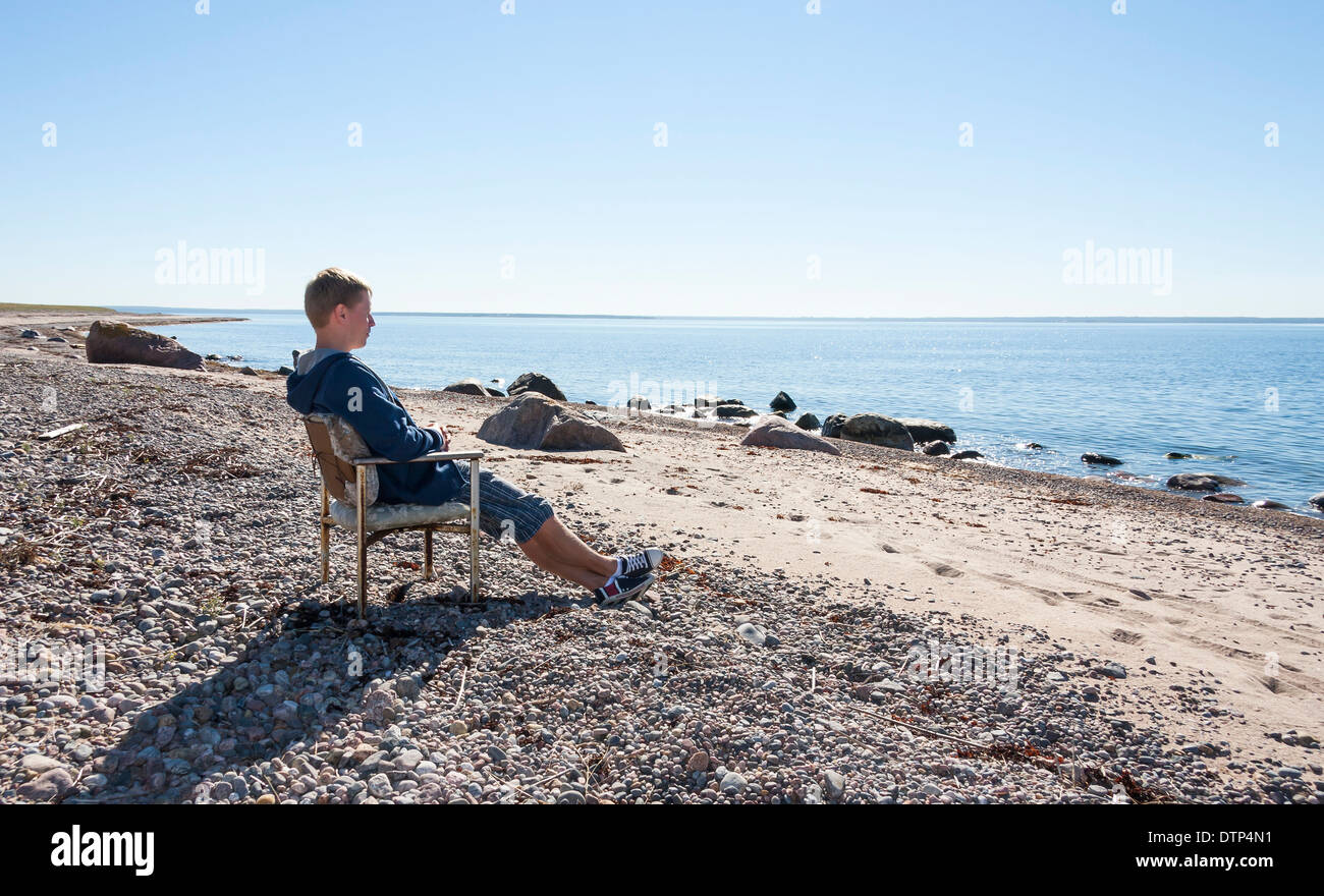 Jungen Erwachsenen Mannes entspannen und sitzen auf Bank in der Nähe von Meer und in Distanz zu beobachten. Stockfoto