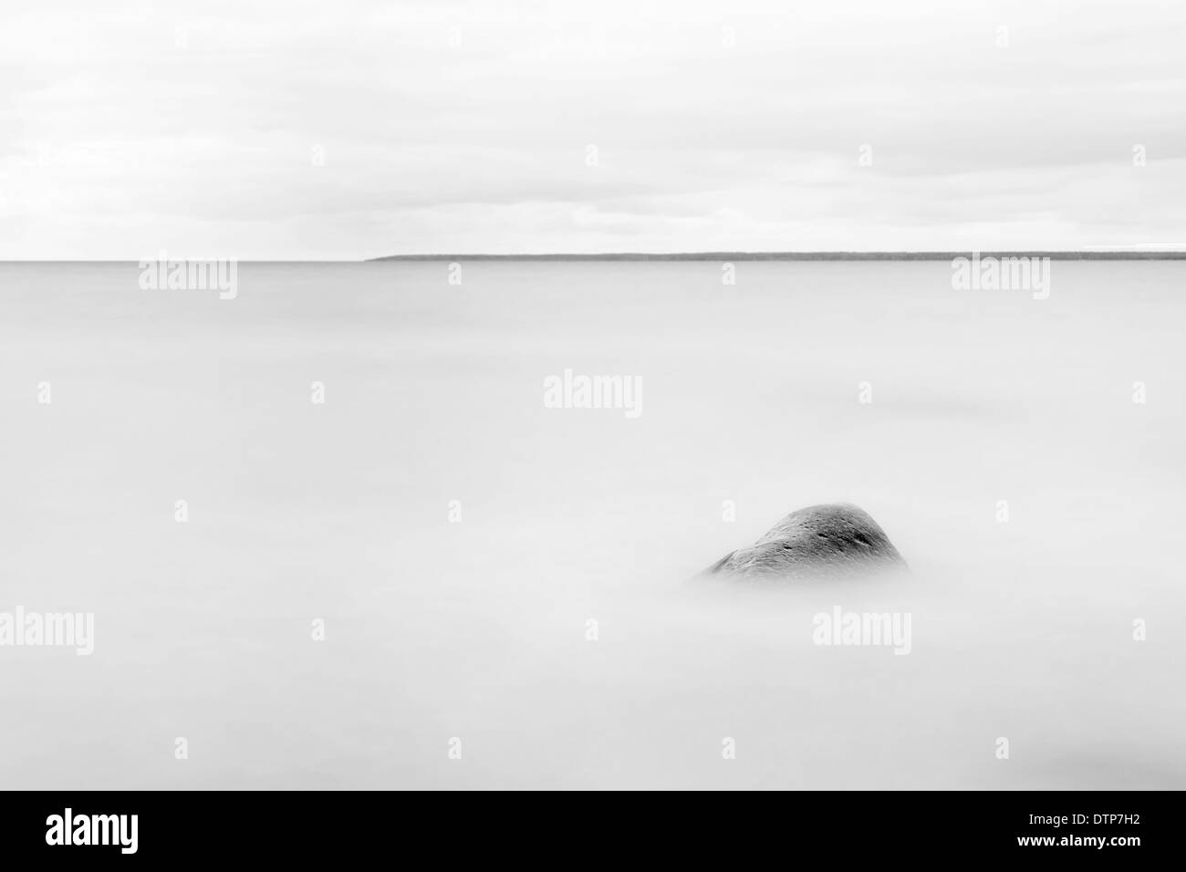 Einzelner Stein oder Fels in einem verschwommenen Meer, Insel im Hintergrund am Horizont Stockfoto