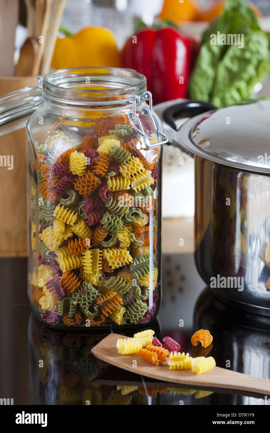 Großer Speicher Jar mit bunten Nudeln und Kochen Löffel mit textfreiraum im oberen und rechten Bereich des Bildes Stockfoto