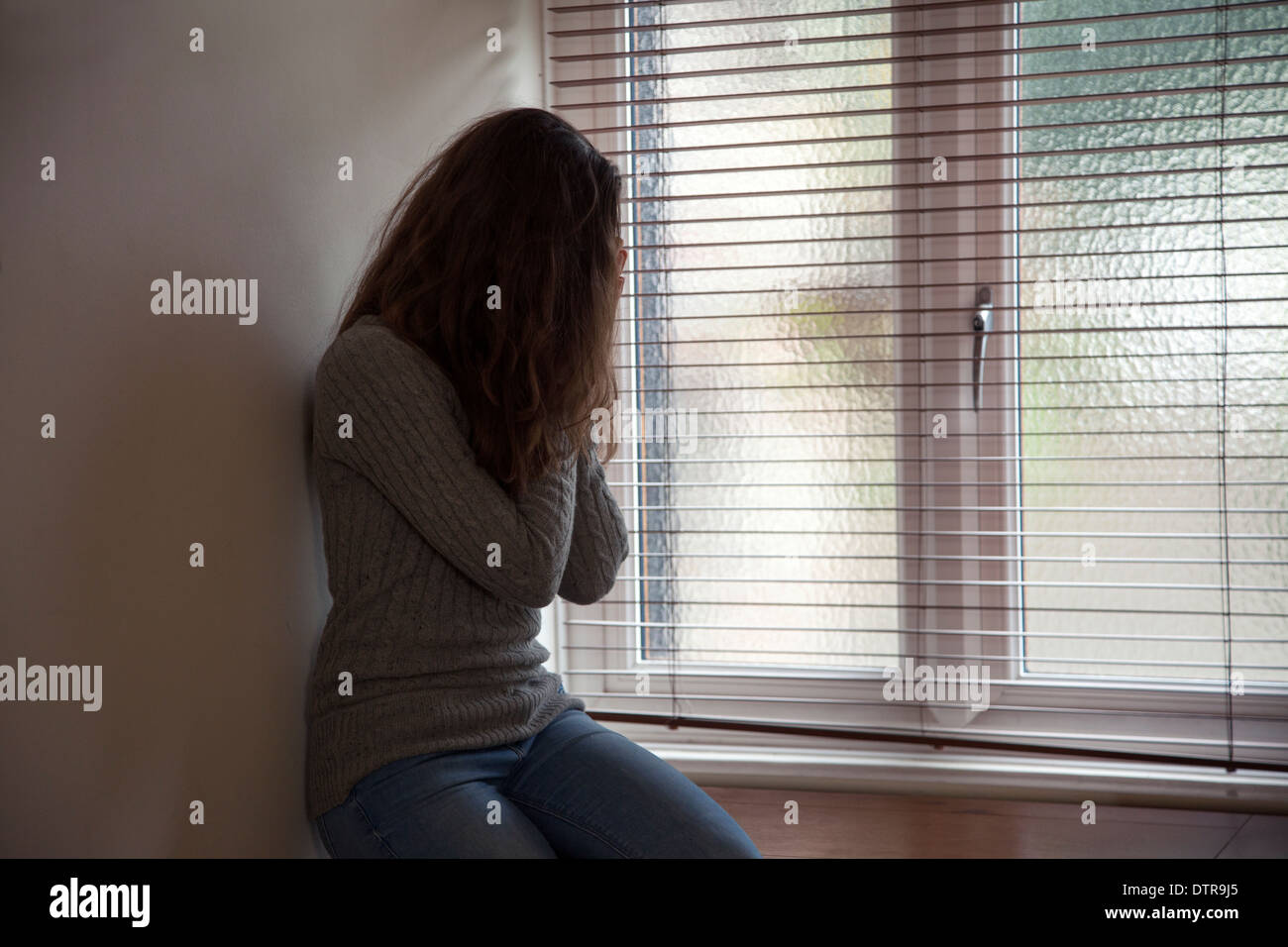 Mädchen mit langen Haaren, die Hände auf ihrem Gesicht, ein Fenster zu Hause sitzen. Seitlichen Aussichtsterrasse. Stockfoto