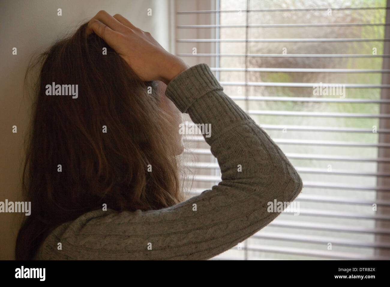 Nicht erkennbare junge Frau mit den Händen auf dem Kopf durch ein Fenster. Stockfoto