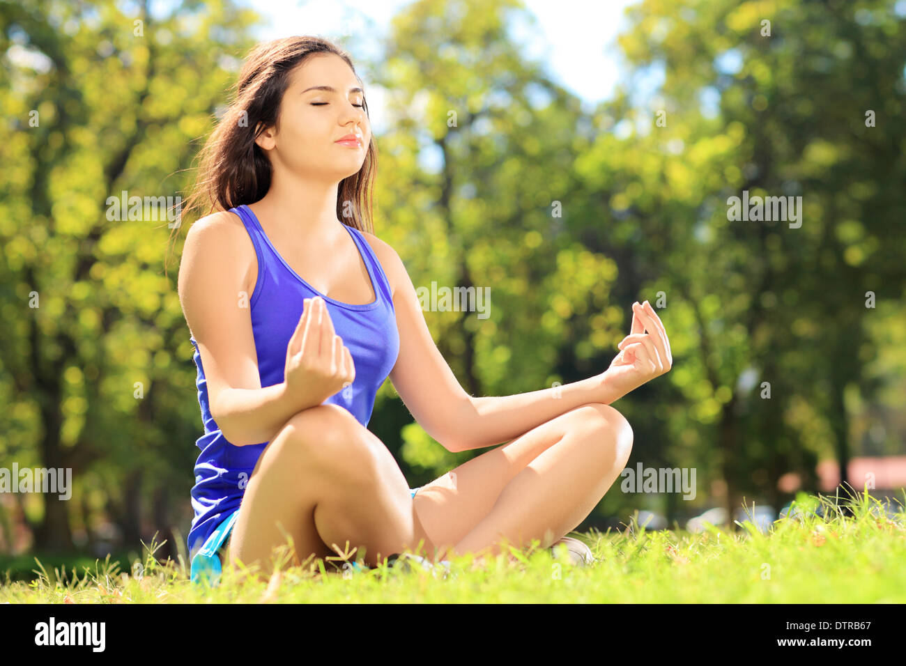 Junge Sportlerin in Sportbekleidung Meditation sitzt auf einer grünen Wiese in einem park Stockfoto