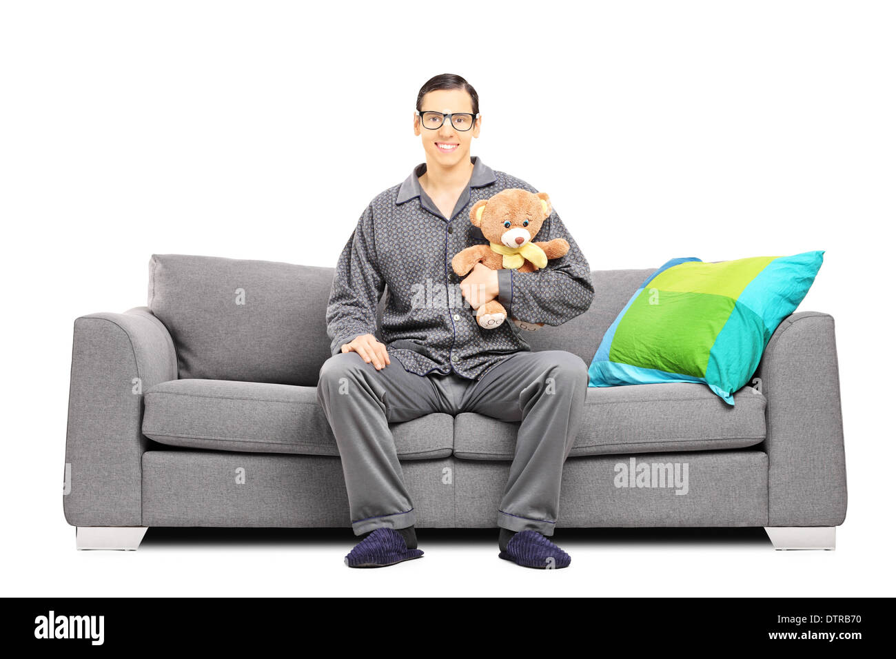 Junger Mann im Schlafanzug auf dem Sofa sitzen und halten einen Teddybär Stockfoto