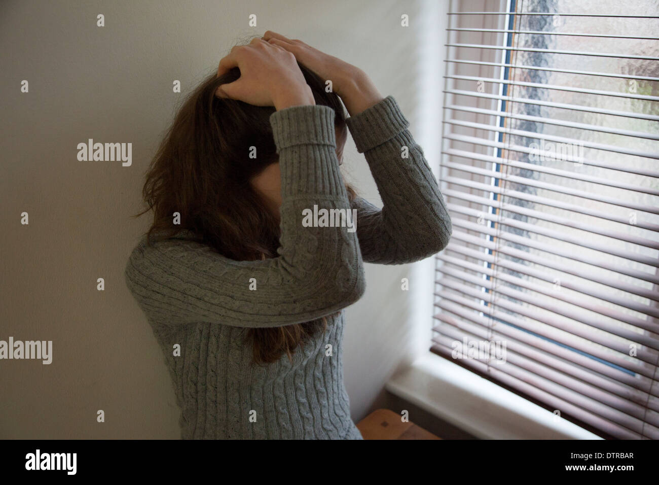 Junge Frau durch ein Fenster die Hände auf ihren Kopf in Verzweiflung. Stockfoto