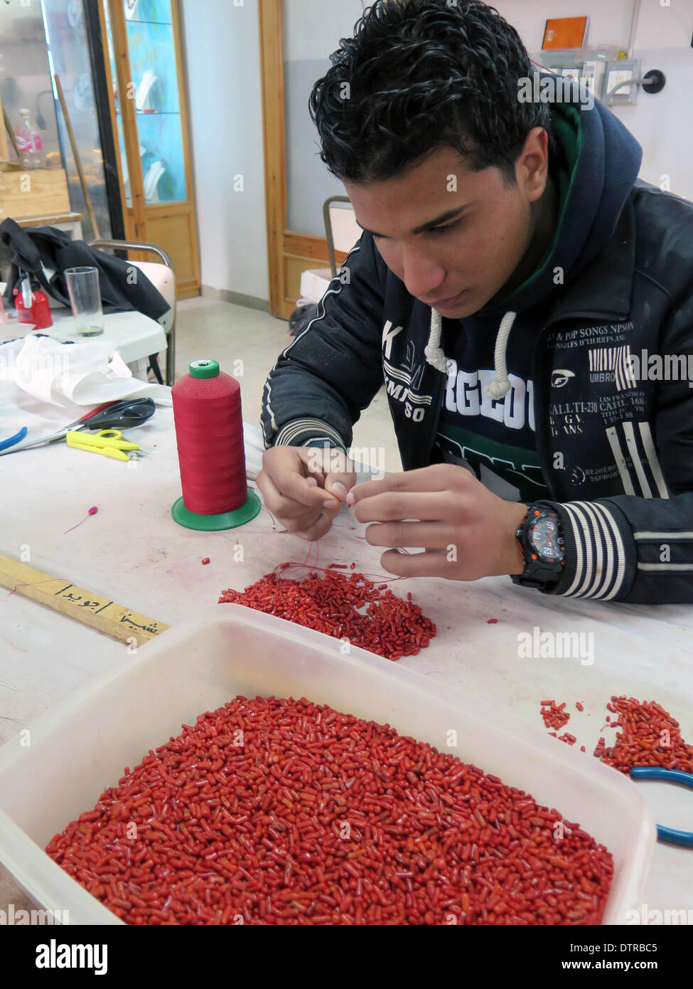 Tunis, Tunesien. 23. Februar 2014. Eine Verkäuferin Fäden rote korallene  Perlen eine Kette in einen Handwerkermarkt in Tunis, Hauptstadt von Tunesien,  23. Februar 2014 machen. Tunesien ist fruchtbar in die Produktion von