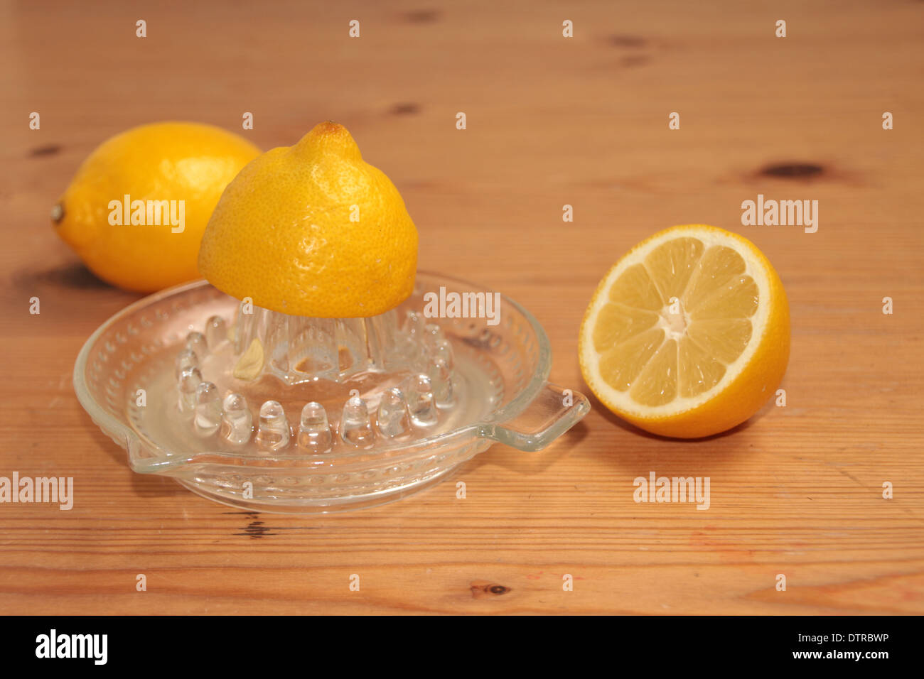 halben Zitrone gequetscht auf ein Glas Saftpresse/Entsafter mit eineinhalb Zitronen im Hintergrund auf Kiefer (2 Reihe von 4) Stockfoto