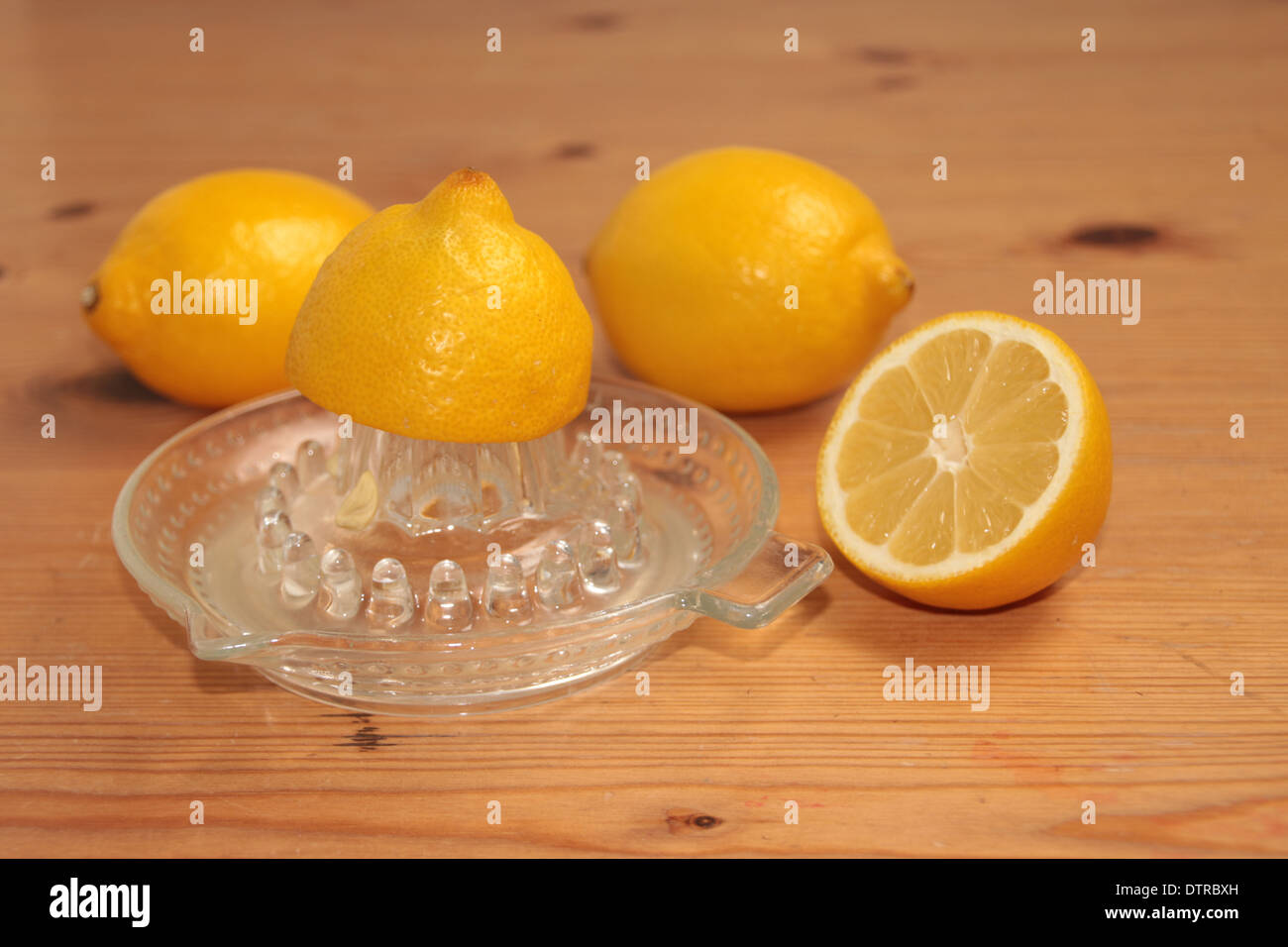 halben Zitrone gequetscht auf ein Glas Saftpresse/Entsafter mit zwei und eine halbe Zitronen im Hintergrund auf Kiefer (3 Serie von 4) Stockfoto