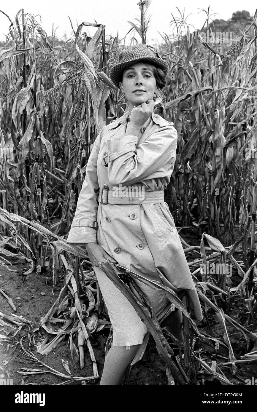 60er Jahre Mode Regenmantel mit Hut posiert in einem Maisfeld Stockfoto