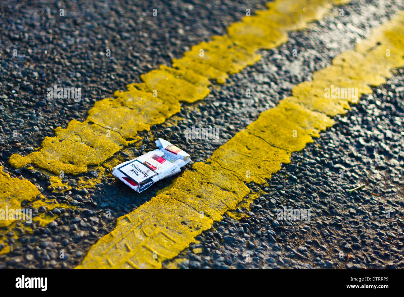 Eine Zigarettenschachtel legt in der Mitte einer Straße zwischen zwei gelben Linien gemalt auf dem Bürgersteig. Stockfoto