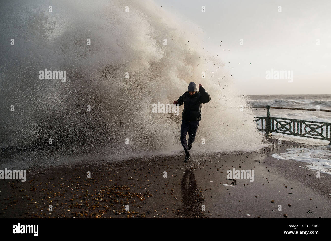 Ein Mann läuft von riesigen Wellen während der Gezeiten Überspannungen auf britischen Küsten bei extremem Wetter. Szene in Brighton, Sussex, Großbritannien Stockfoto