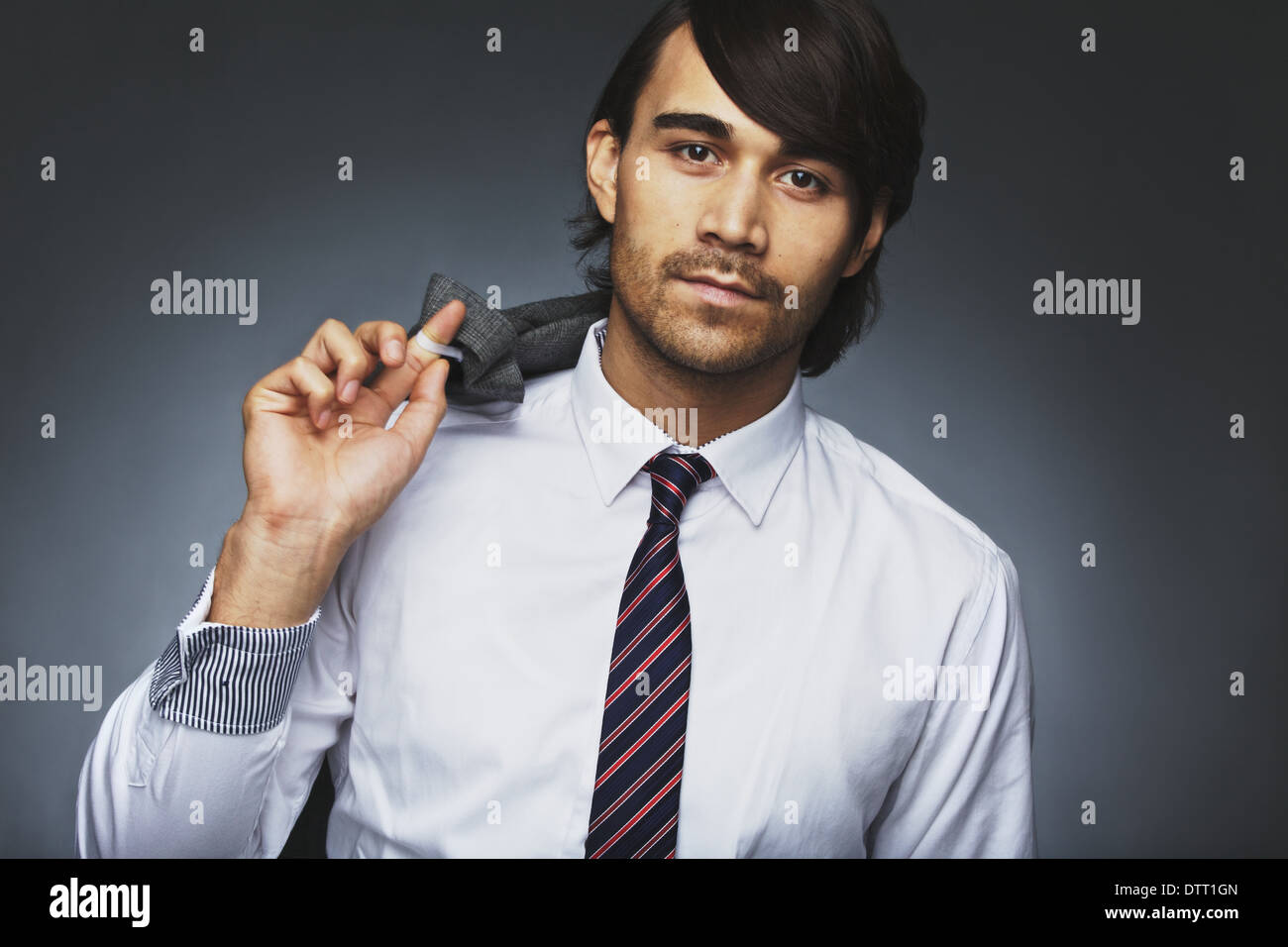 Porträt von attraktiven jungen Mann in formelle Kleidung posiert vor grauem Hintergrund. Junger Geschäftsmann hält seine Jacke. Stockfoto
