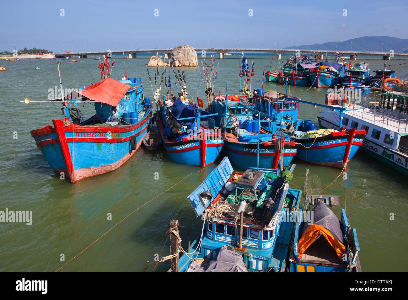 Hübsche blaue Angelboote/Fischerboote vor Anker in der Bucht mit Hauptküstenstraße Brücke jenseits von Nha Trang, Provinz Khanh Hoa, Vietnam Stockfoto