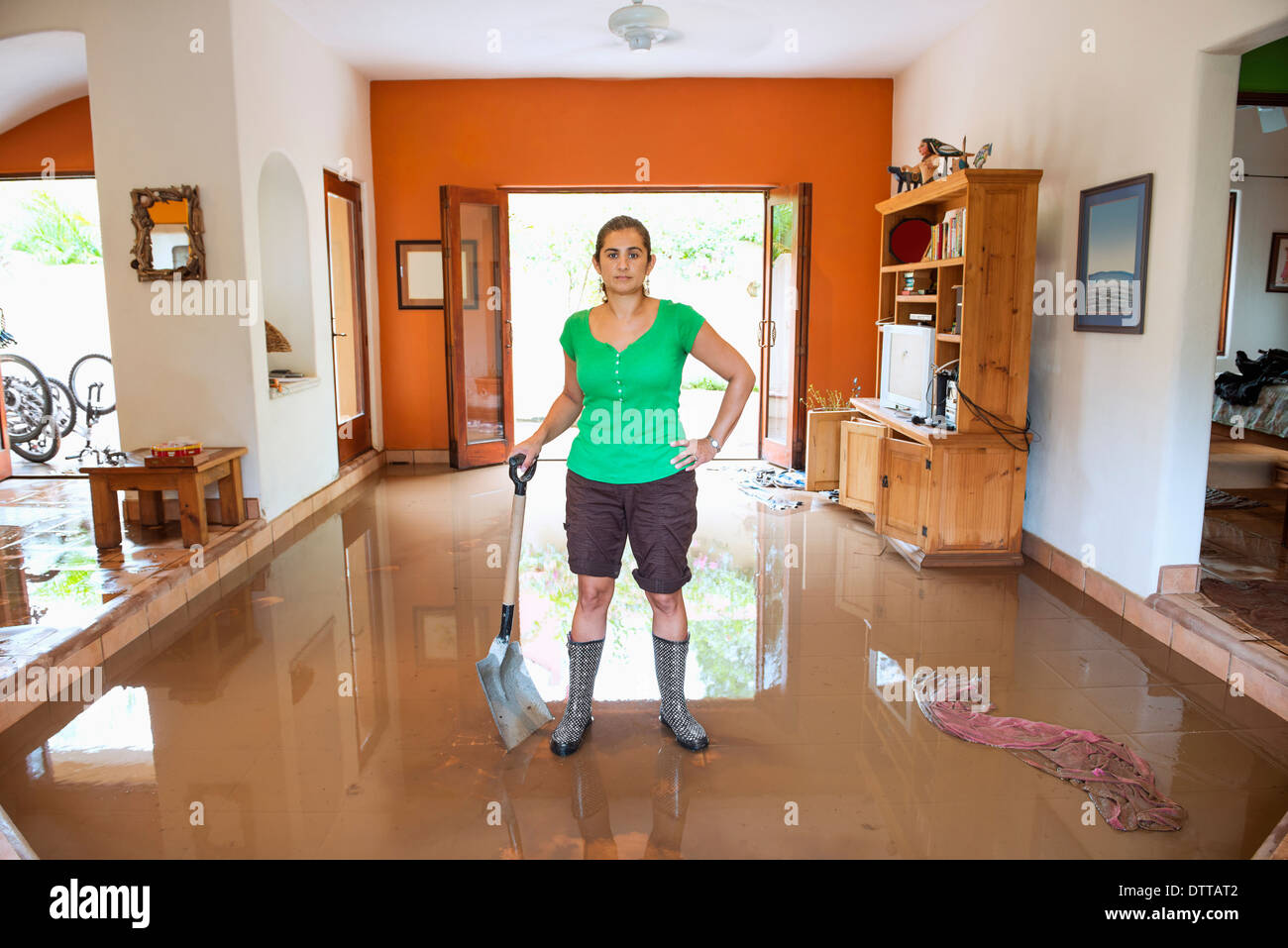 Hispanic Frau Schaufeln Wasser aus überfluteten Haus Stockfoto