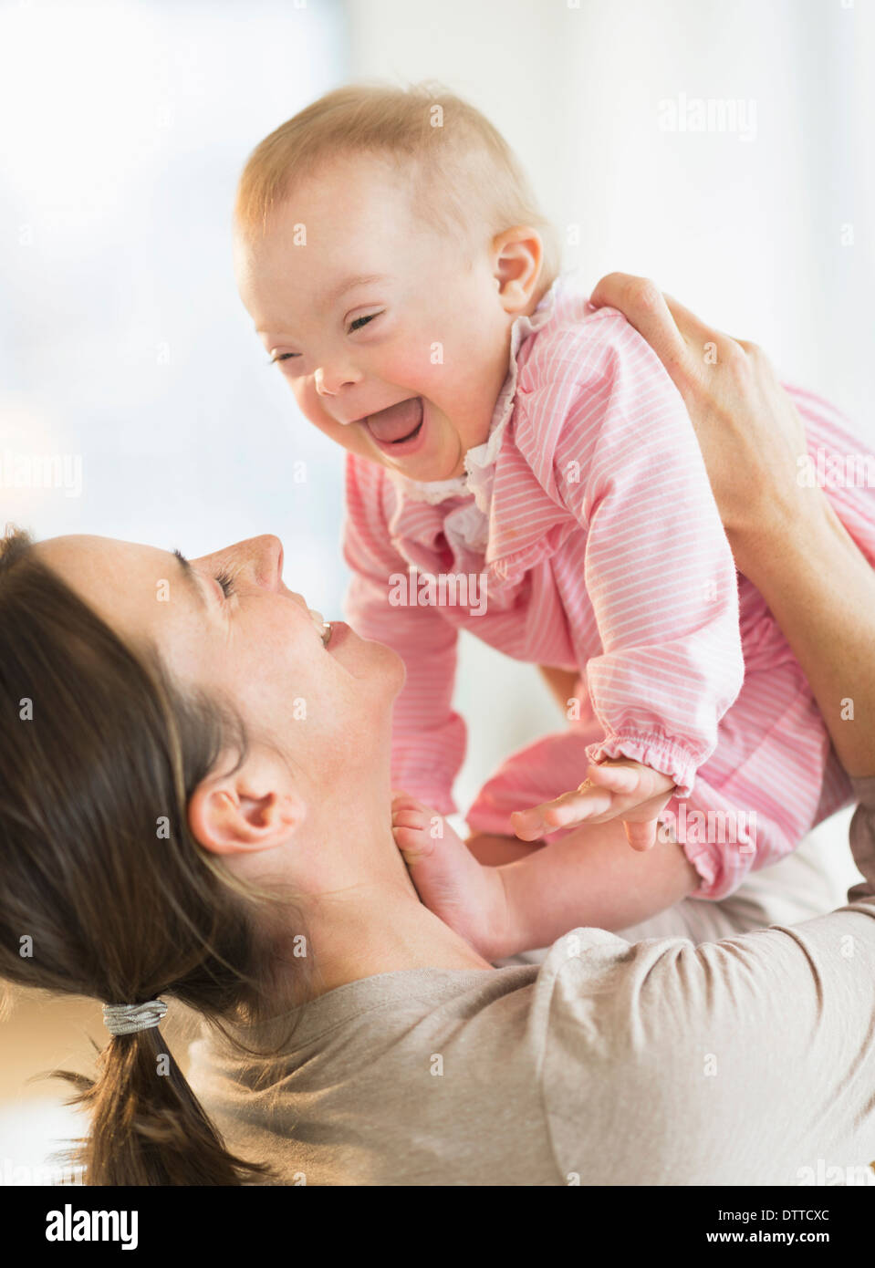 Kaukasische Mutter spielen mit Babymädchen mit Down-Syndrom Stockfoto