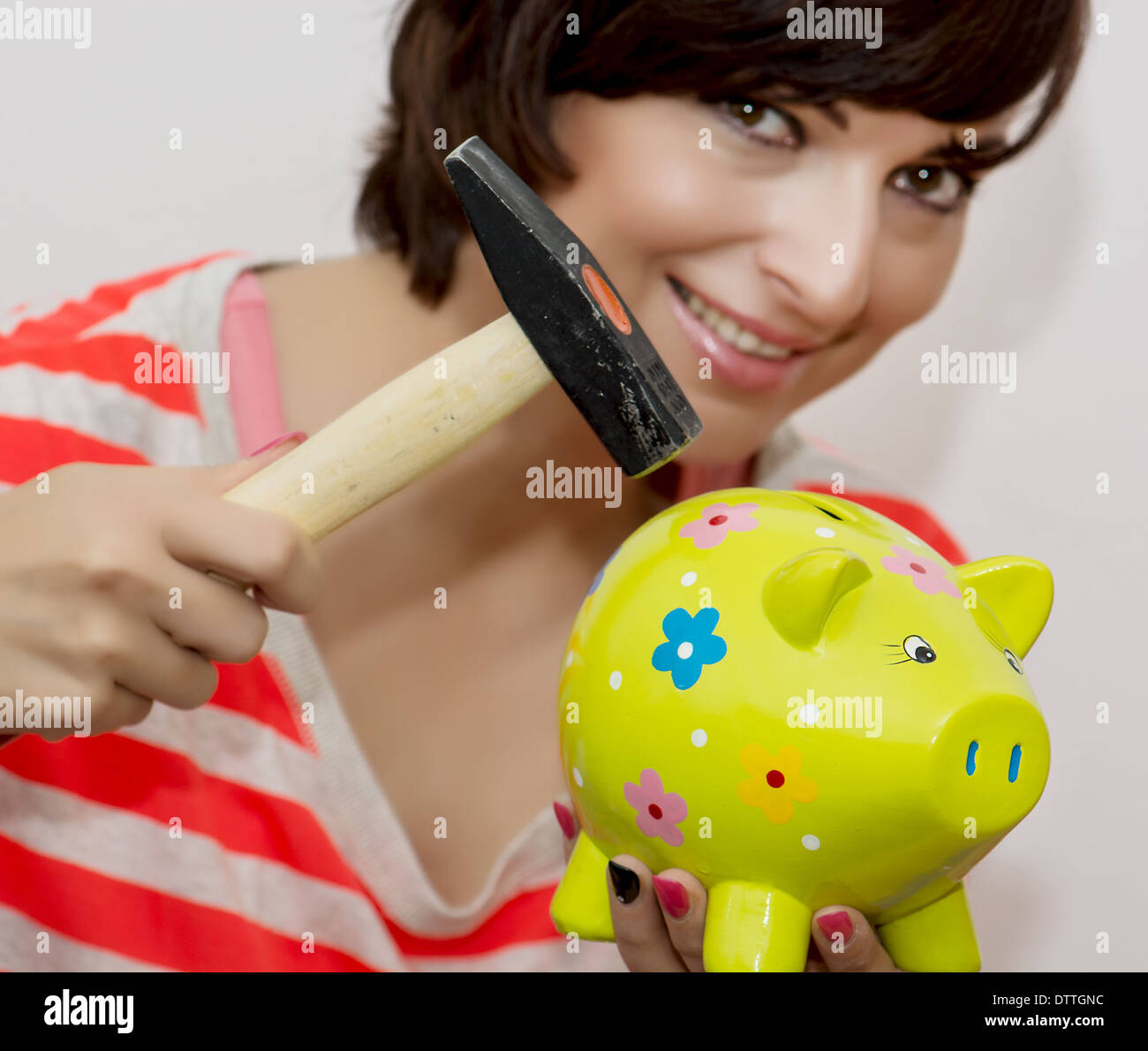 Lächelnde junge Frau bricht ein Porzellan Sparschwein mit einem Hammer. Stockfoto