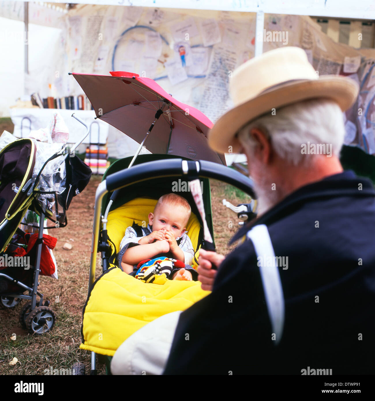 Großvater mit Strohhut, Babysitter, während das Baby seinen Zeh lutscht, beim Hay-on-Wye-Wales-Festival im Kinderwagen, Großbritannien, KATHY DEWITT Stockfoto