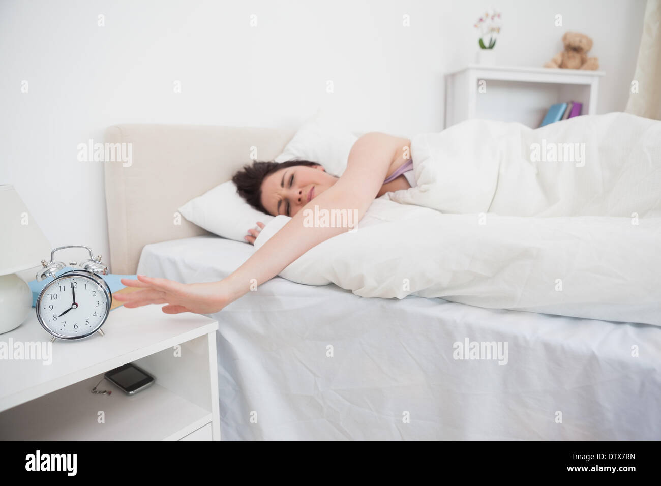 Verschlafene Frau streckte Hand mit Wecker Stockfoto