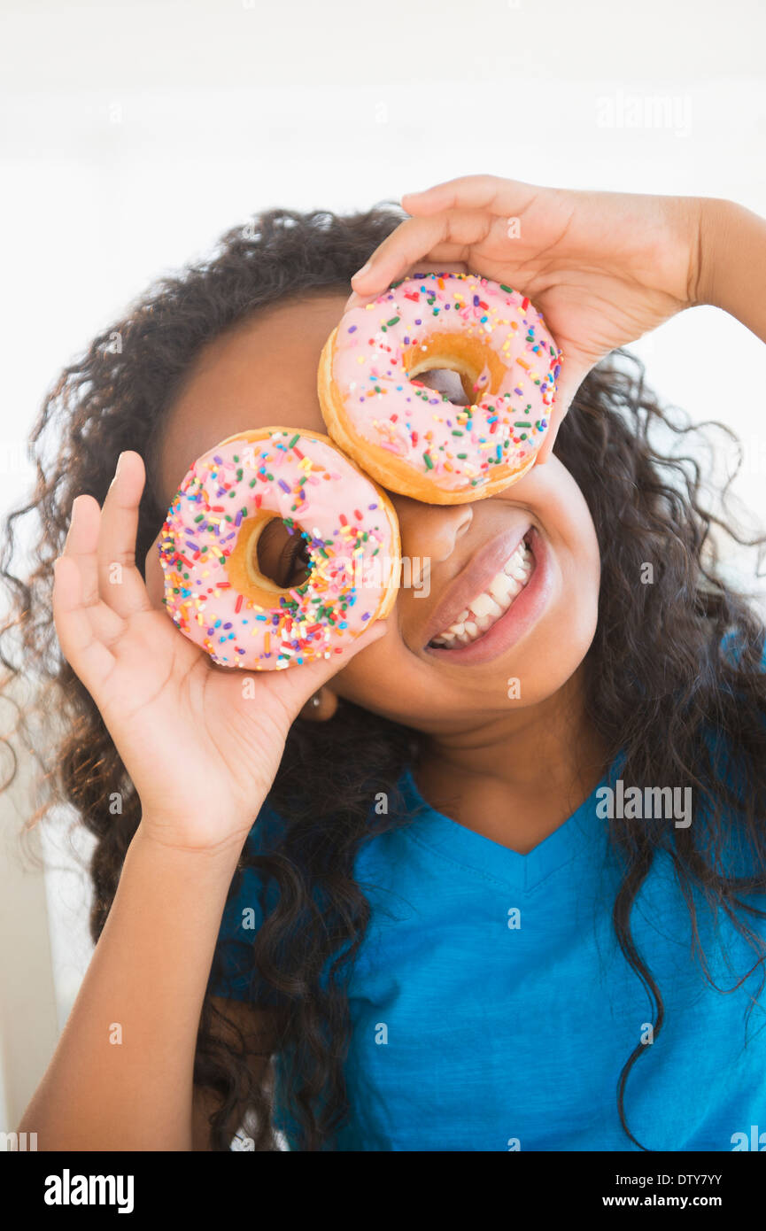 Gemischte Rassen Mädchen hält Donuts über ihre Augen Stockfoto