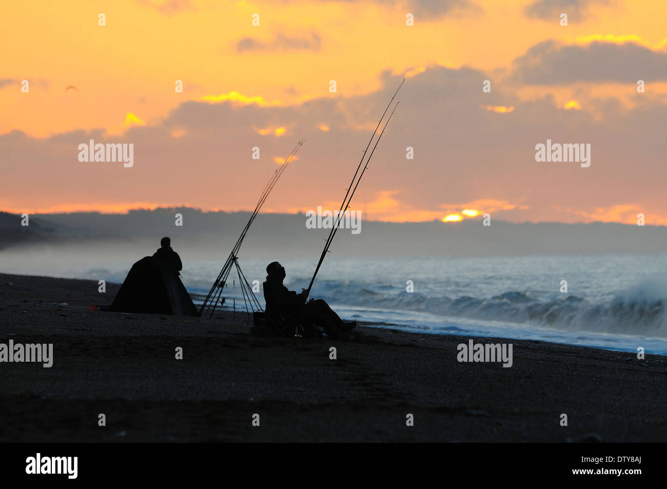 Zwei Fischer in der Morgendämmerung mit ihren Stäben, sitzen, warten am Meer UK Stockfoto