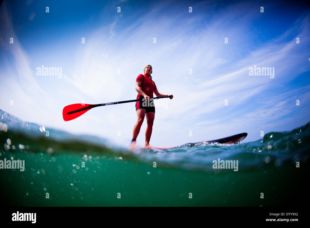 Ein Mädchen in einem roten Ausschlag Weste Paddleboards in den klaren Gewässern von North Devon UK SUP (Stand up Paddling) Stockfoto