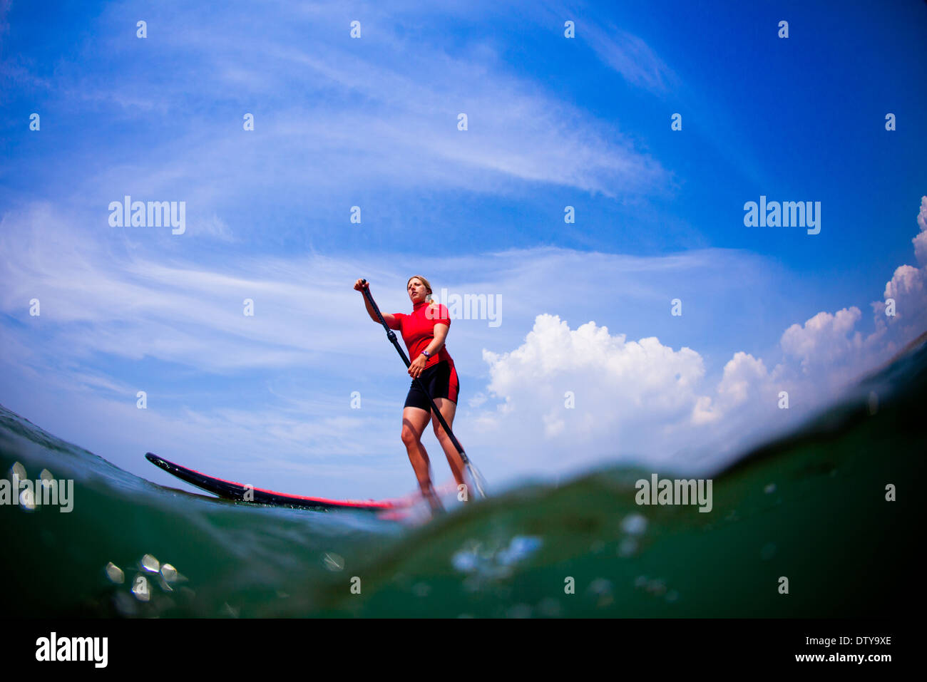 Ein Mädchen in einem roten Ausschlag Weste Paddleboards in den klaren Gewässern von North Devon UK SUP (Stand up Paddling) Stockfoto