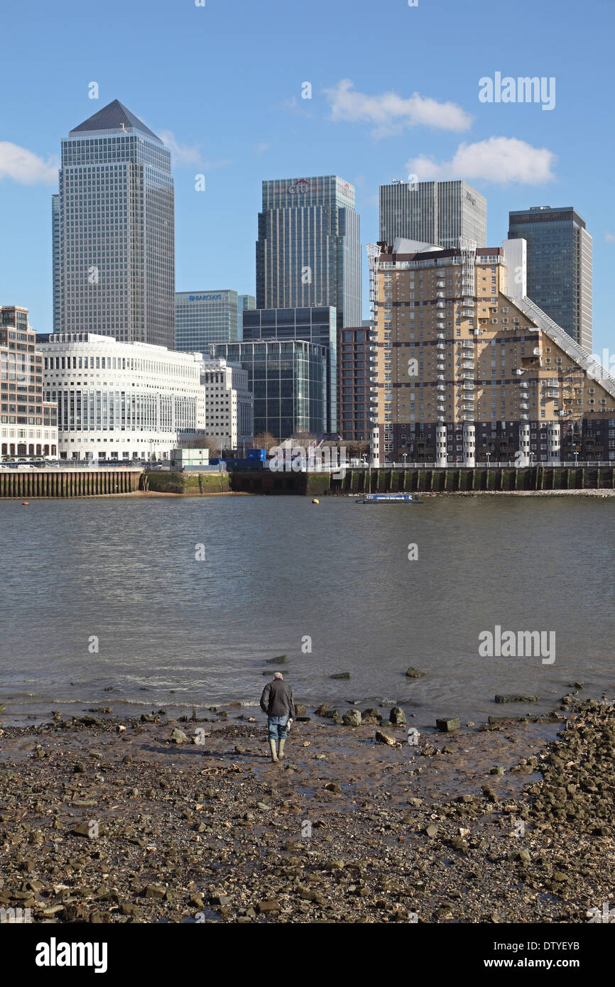 Ein Mann geht am Rand Wassers von der Themse bei Ebbe mit der Londoner Canary Wharf Entwicklung im Hintergrund Stockfoto