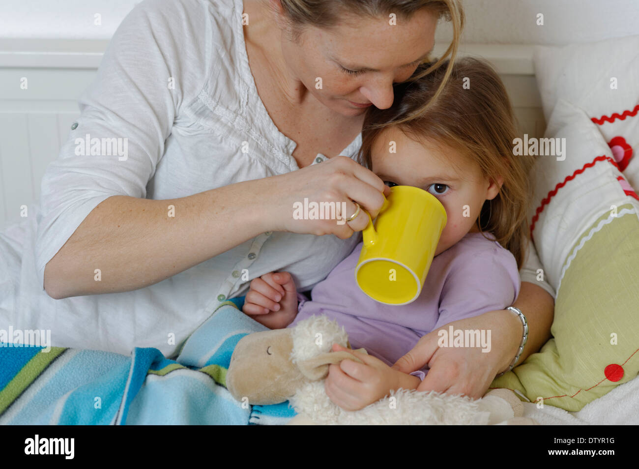Mutter kümmert sich um ihre kranke Tochter, Verzicht auf heißen Tee, Mädchen im Bett liegend Stockfoto