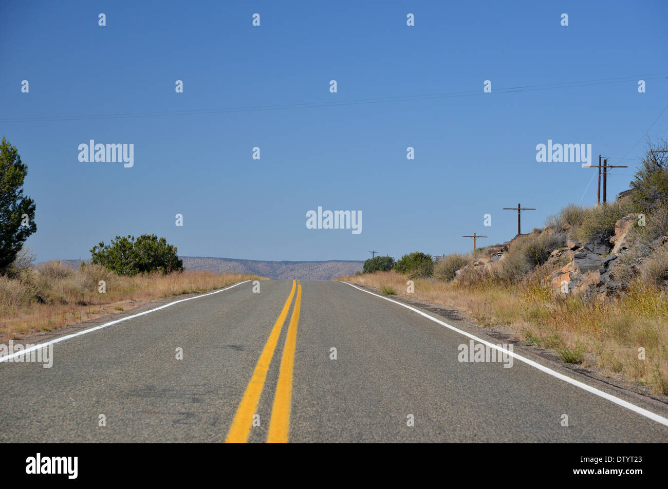 Route 66, USA. Langen, geraden Straße verschwindet über den Kamm in Richtung Berge unter blauem Himmel einsam Stockfoto