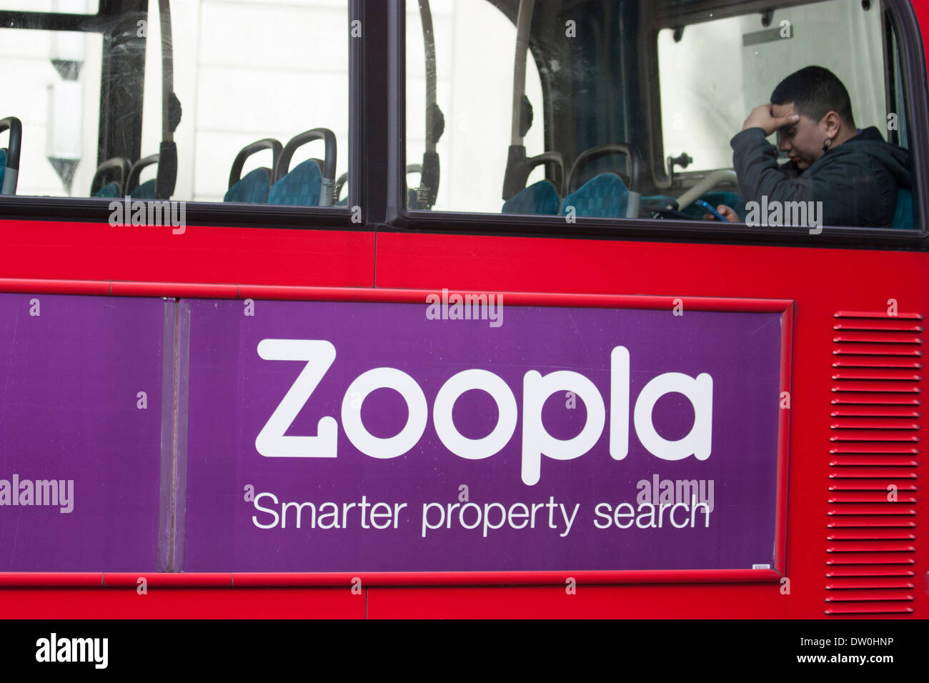 Mann saß auf dem Oberdeck eines Londoner Busses und schaute auf sein Handy, mit einer Zoopla-Immobilienanzeige an der Seite des Fahrzeugs. Aufgenommen in der City of London, Großbritannien – ein Moment des täglichen städtischen Lebens und des digitalen Engagements in der Hauptstadt Stockfoto