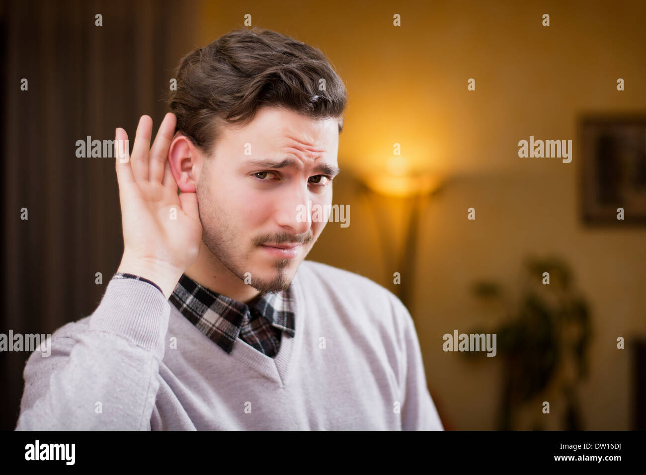 Hübscher junger Mann kann nicht hören, legte die Hand um ihm ins Ohr. Drinnen im Inneren eines Hauses erschossen Stockfoto