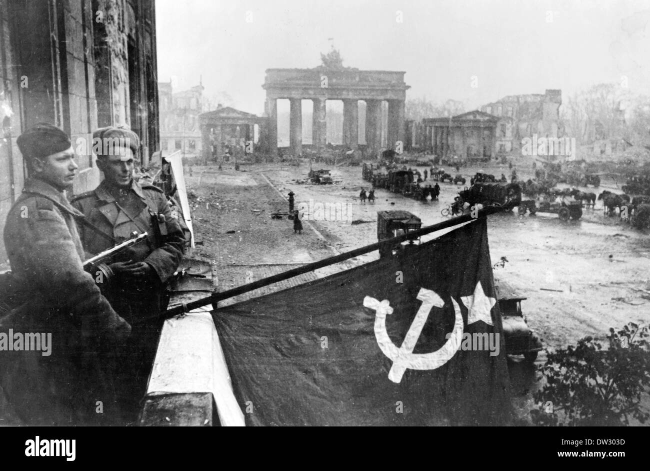 Ende des Krieges in Berlin 1945 - Soldaten der Roten Armee hissen die sowjetische Flagge von einem Balkon des berühmten Hotel Adlon vor sowjetischen Einheiten, die sich am Brandenburger Tor in Berlin versammeln. Fotoarchiv für Zeitgeschichte - KEIN KABELDIENST Stockfoto