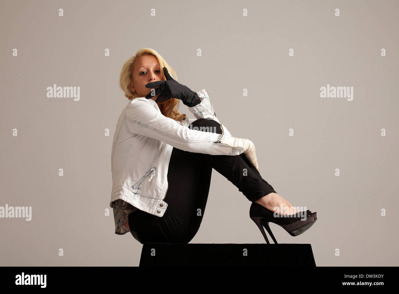 horizontalen Schuss eleganten jungen Frau mit high Heels, Jean Jacke und schwarze Hose verstecken ihr Gesicht hinter der hand Stockfoto