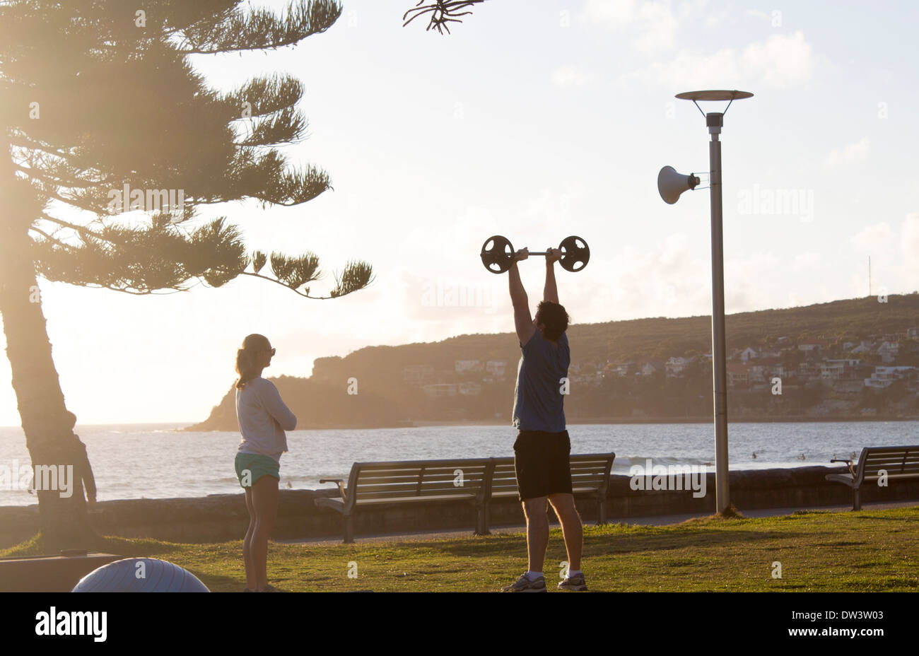 Mann, Gewichte zu heben beobachtet von weiblichen Personaltrainer am frühen Morgen Trainingseinheit Manly Sydney NSW Australia Stockfoto