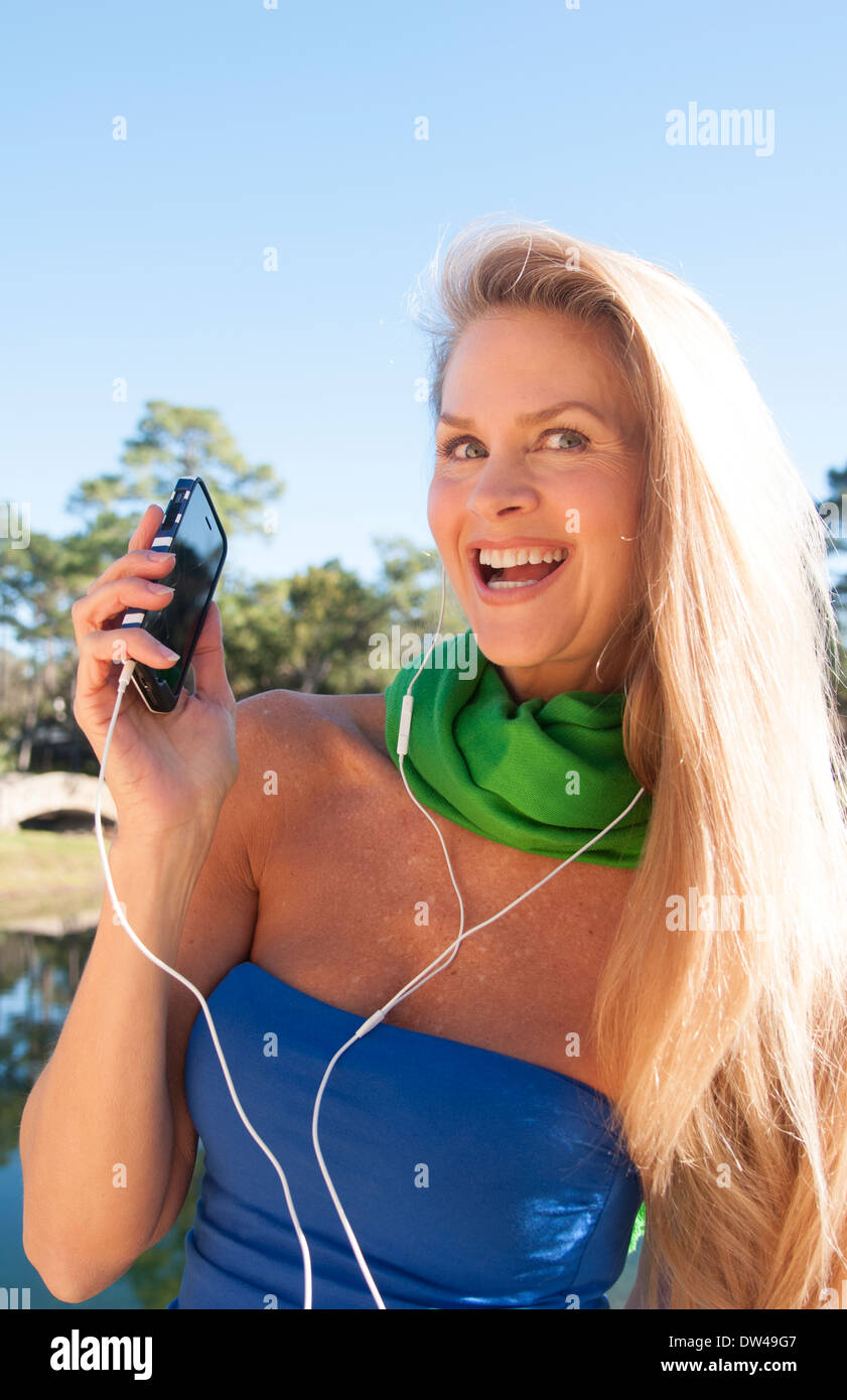 junge attraktive 50-jährige Frau anhören von Musik auf Handy-Lächeln im Freien noch schöner noch im mittleren Alter Stockfoto
