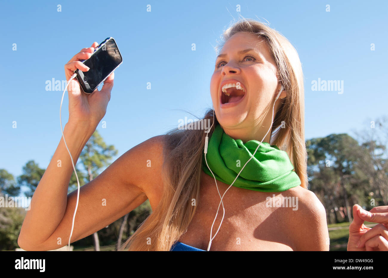 junge attraktive 50-jährige Frau anhören von Musik auf Handy-Lächeln im Freien noch schöner noch im mittleren Alter Stockfoto