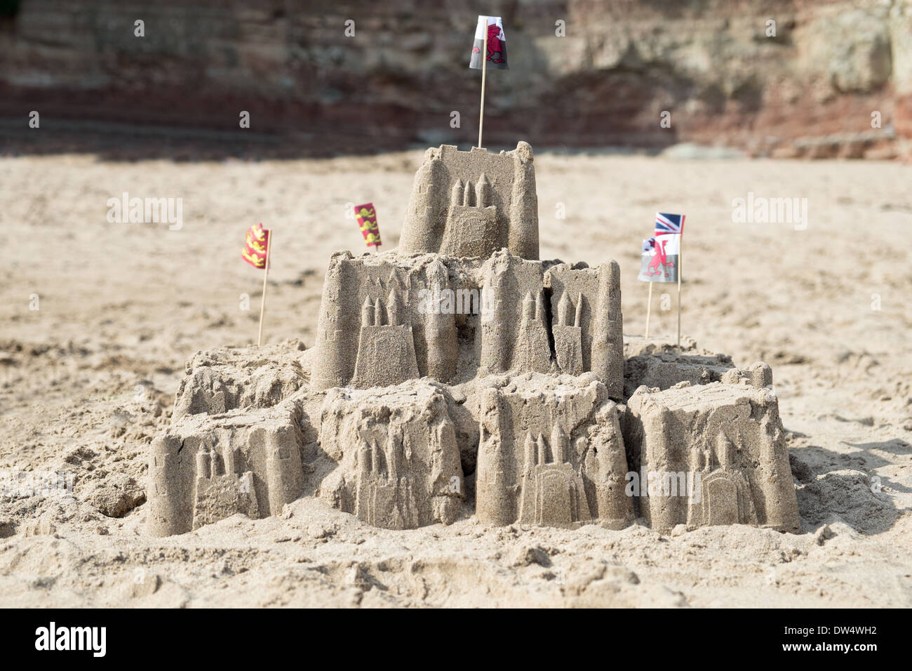 An einem Sandstrand eine Sandburg gekrönt mit der Welsh national andere britische Flaggen Stockfoto