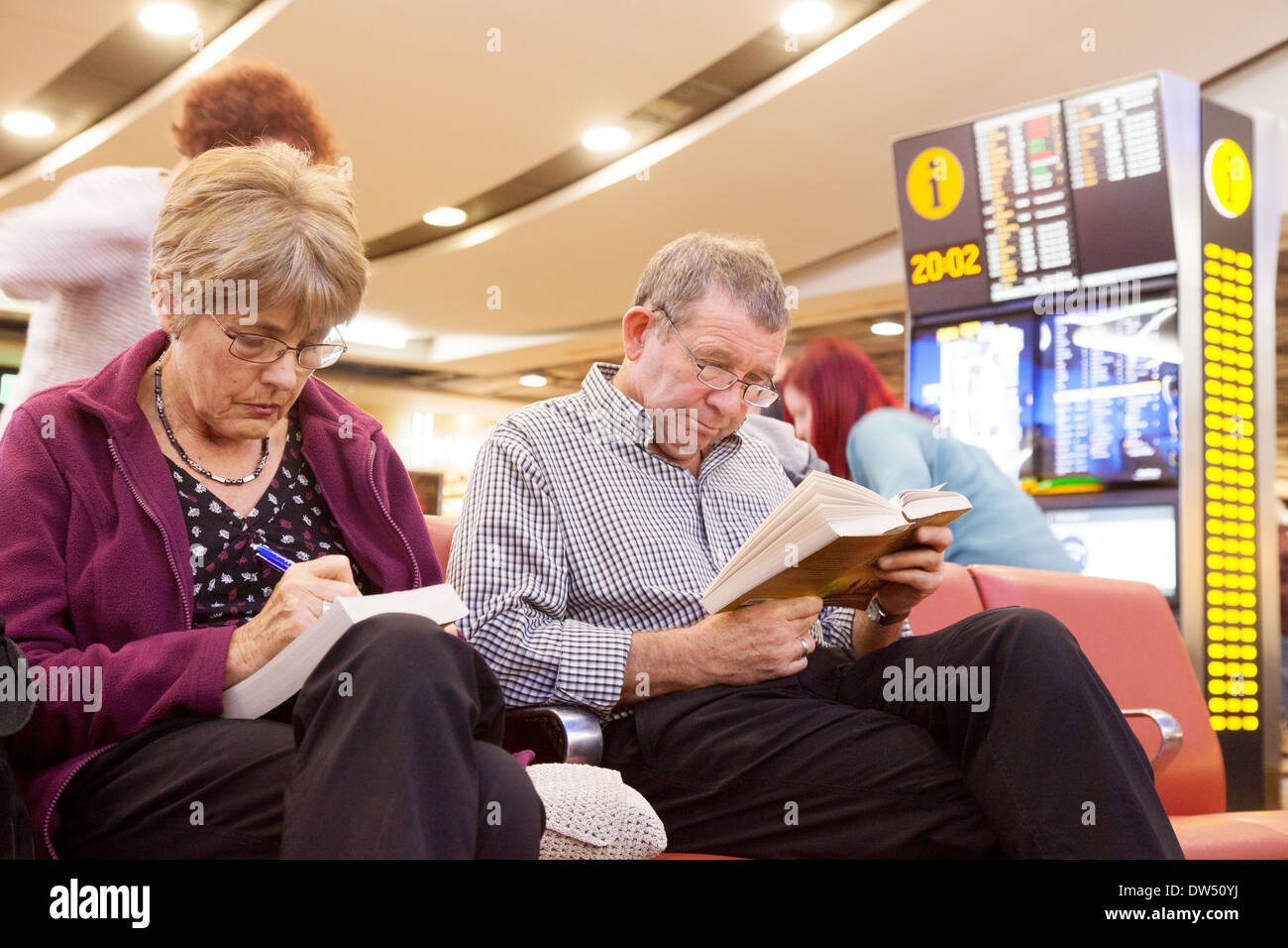 Die Fluggäste lesen und schreiben in der Abflughalle warten auf ihren Flug, Terminal 3, Flughafen Heathrow London UK Stockfoto