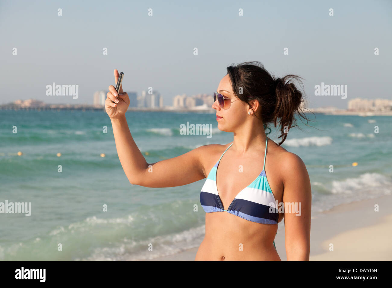 Frau fotografieren Selfie am Strand im Bikini, im Urlaub, Jumeirah Beach, Dubai, Vereinigte Arabische Emirate, Vereinigte Arabische Emirate, Naher Osten Stockfoto