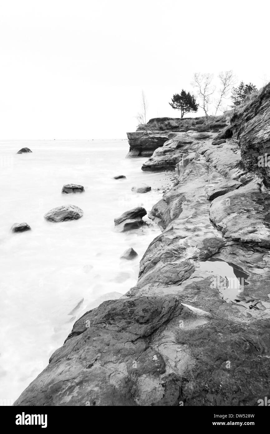 Klippe in der Nähe von Meer und einige Felsen im Wasser an einem bewölkten Tag Stockfoto