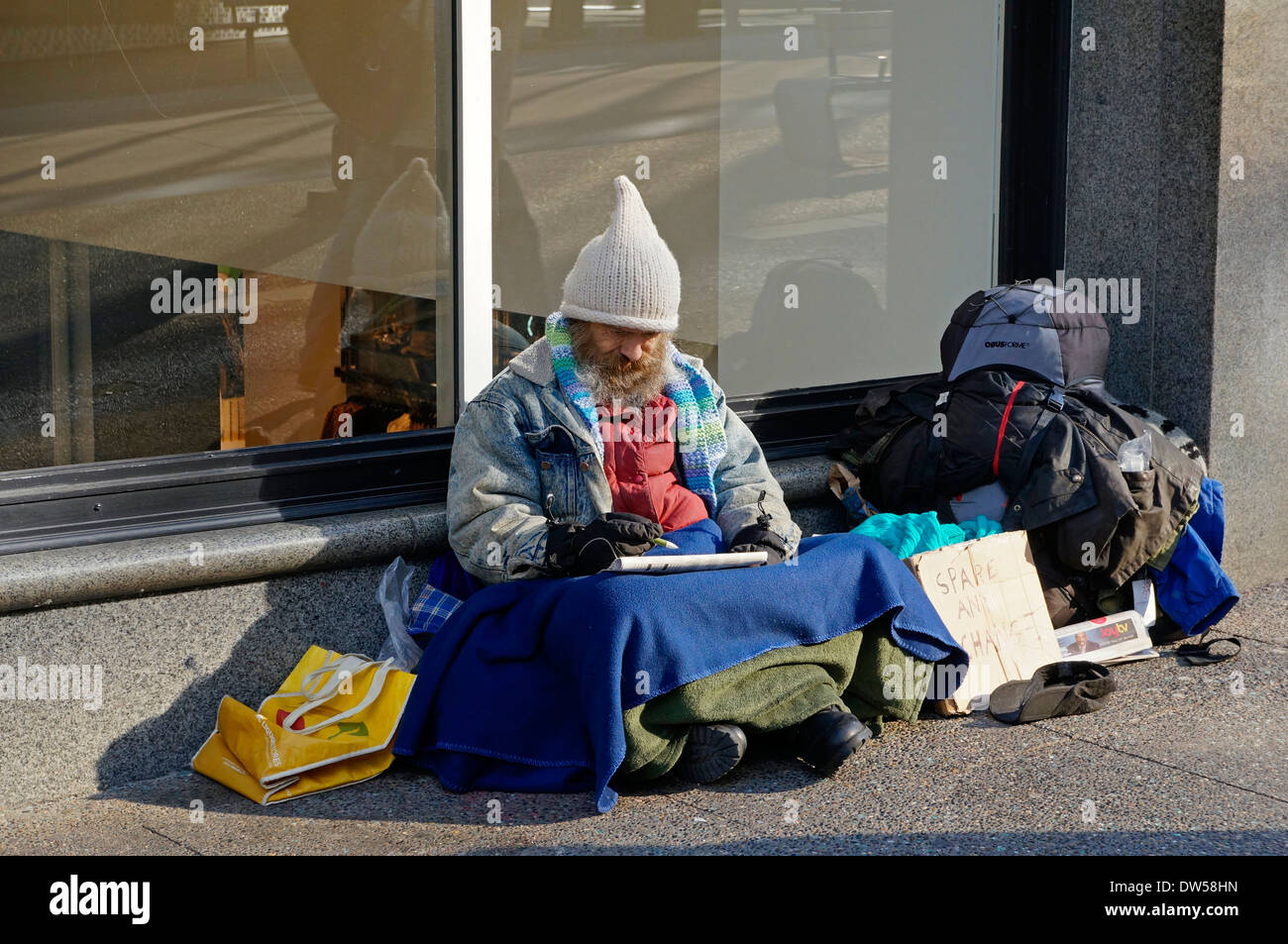 Bärtige Obdachloser auf dem Bürgersteig sitzen und dabei ein Kreuzworträtsel auf Granville Street, Vancouver, BC, Kanada Stockfoto