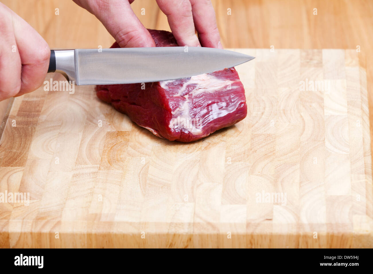 Auf ein rohes Stück Rinderfilet wird das Fett mit einem Küchenmesser abgeschnitten Stockfoto