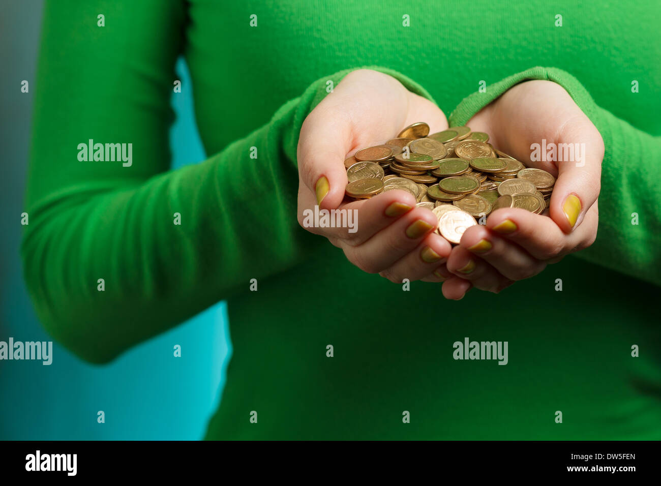 Mädchen im grünen Rollkragenpullover mit Goldmünzen in Händen auf grüne Grunge Hintergrund isoliert Stockfoto