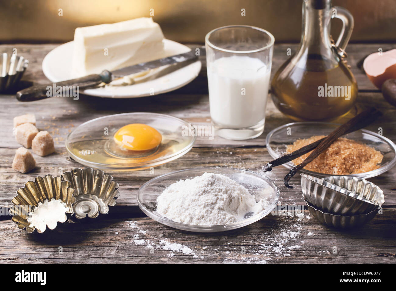 Zutaten für das Backen (Mehl, Ei, brauner Zucker, Milch) mit Vintage Cupcake Formen auf alten Holztisch. Stockfoto