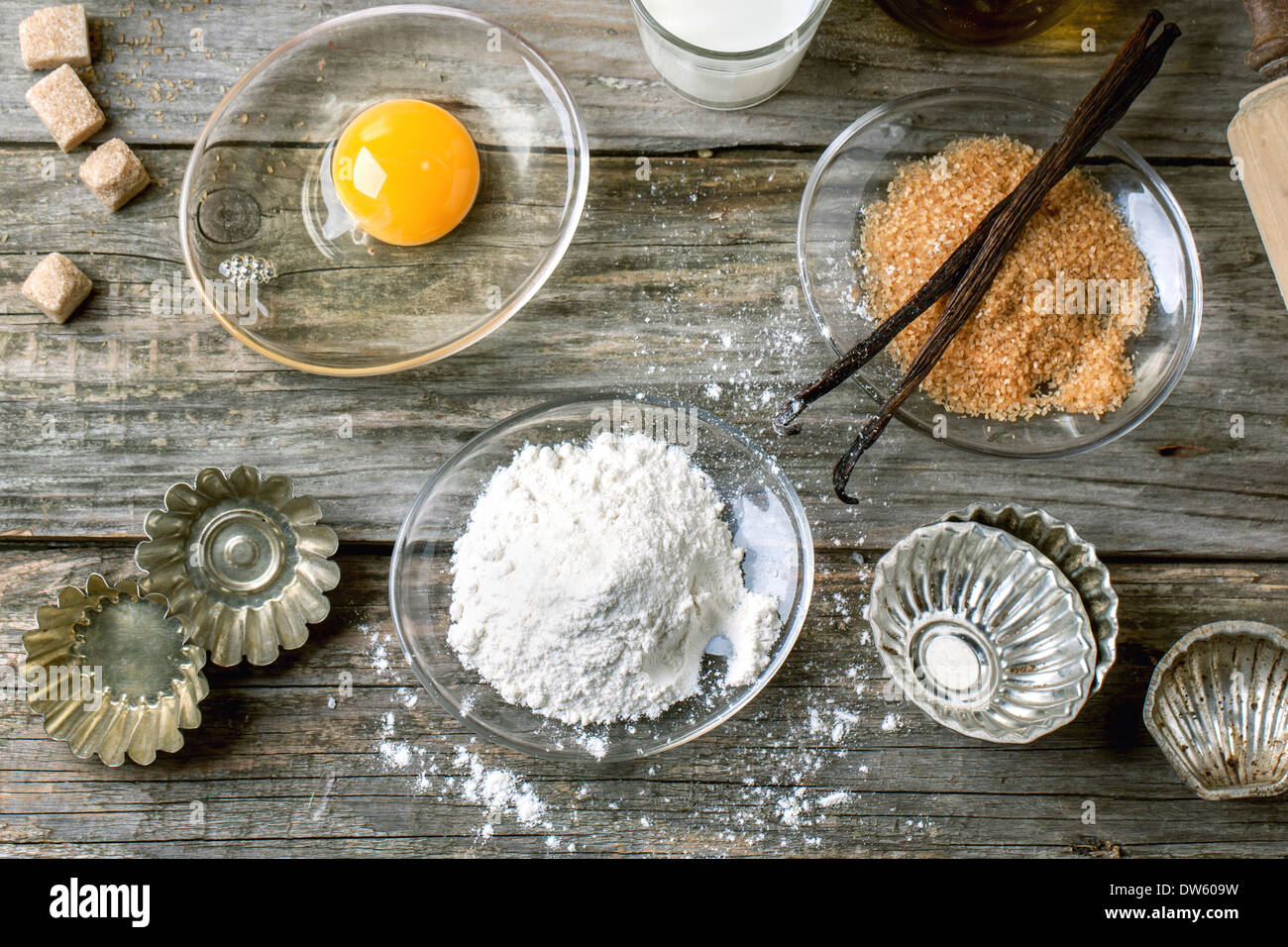 Draufsicht auf Zutaten zum Backen (Mehl, Ei, brauner Zucker, Milch) mit Vintage Cupcake Formen auf alten Holztisch. Stockfoto