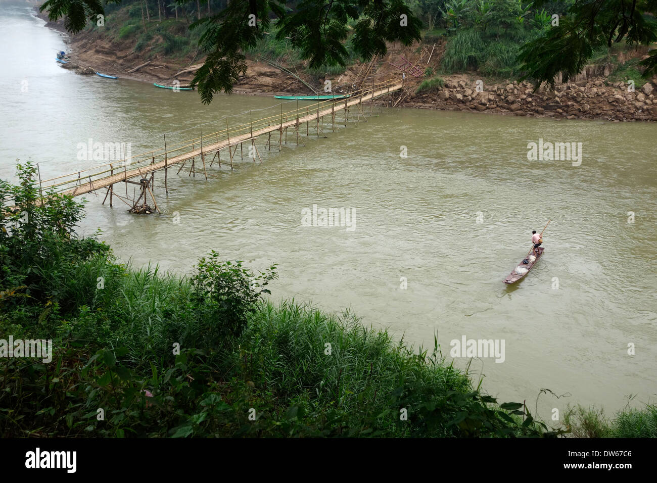 Laotische Fischer poling sein Boot über die saisonalen Bambusbrücke am Fluss Nam Kahn in Luang Prabang, Laos. Stockfoto