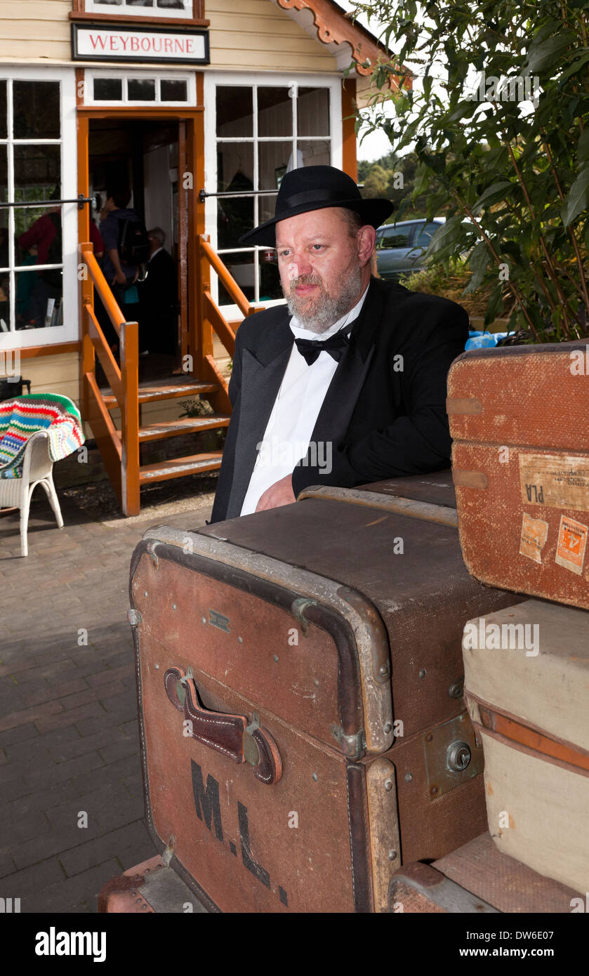 Ein Mann in vierziger Jahre Kostüm stützte sich auf etwas Gepäck am Bahnhof Weybourne Stockfoto