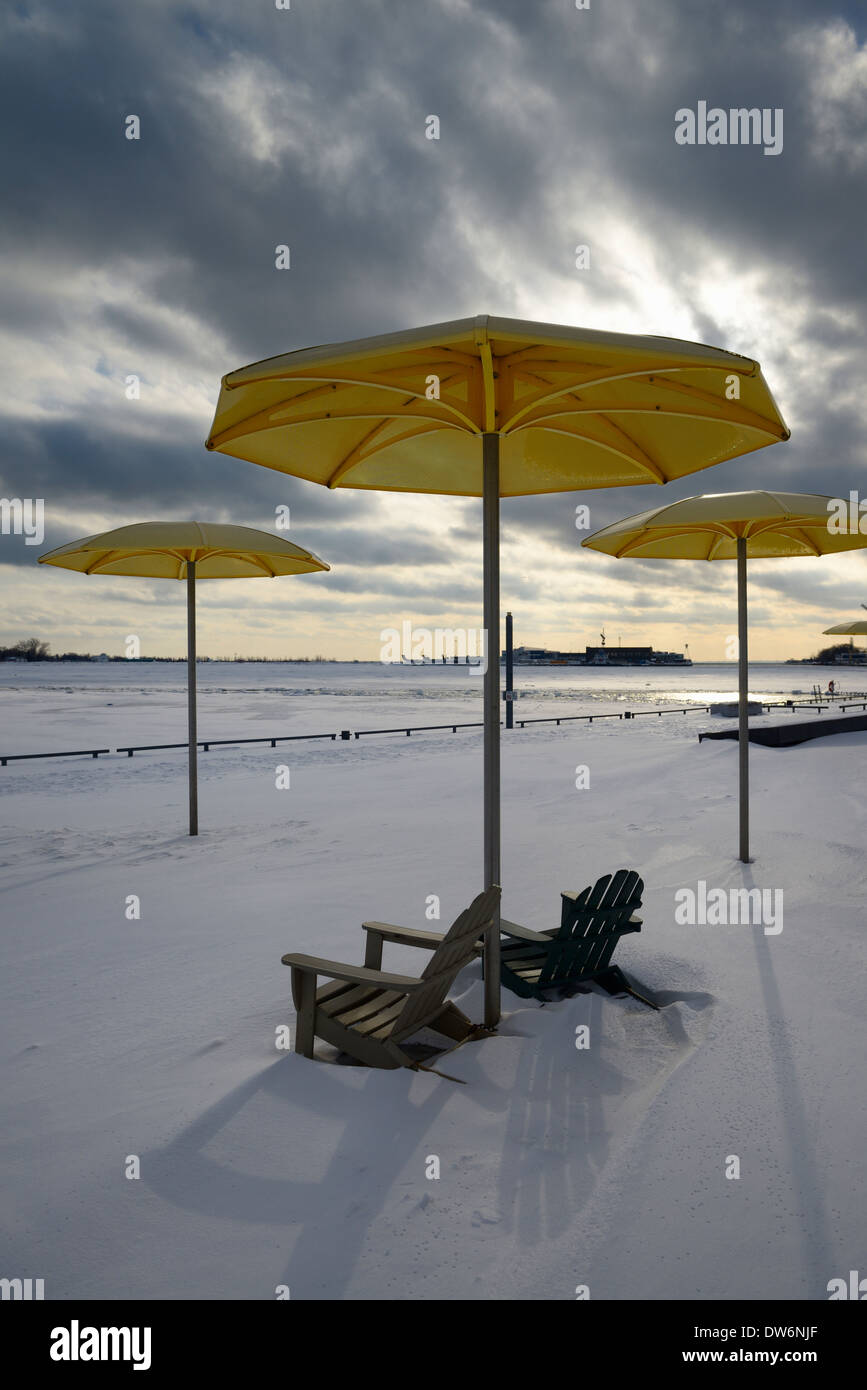 Schneebedeckte Harbourfront HTO Urban Park Strand mit gelben Sonnenschirmen und Muskoka Stühle mit Winter und Toronto Island Airport Stockfoto